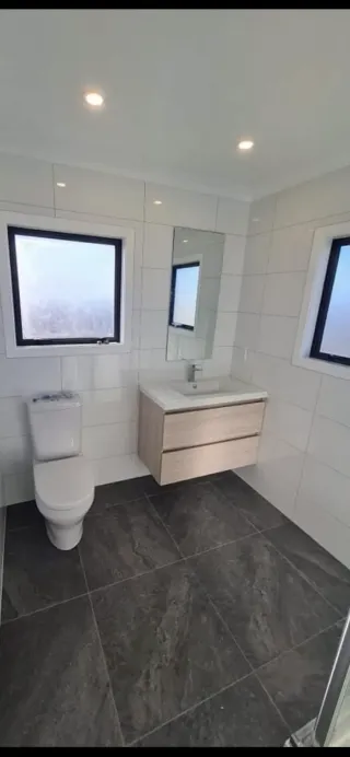 Modern bathroom with wooden vanity, black framed windows and frameless shower